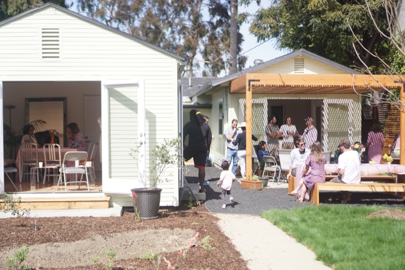 Visitors gathered in the studio and under the pergola on a bright open-garden day.