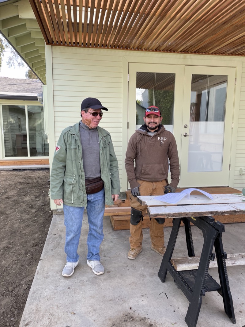 Two of the builders at a sawhorse workbench on the new patio, plans spread out in front of them.